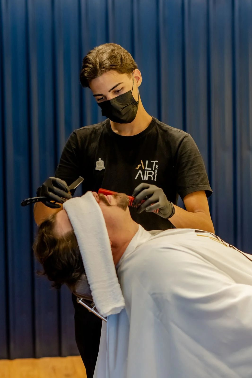 Barbeiro de máscara fazendo a barba de um cliente